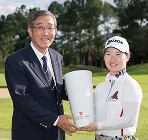 【代表取締役社長】小手川 強二と【優勝】石川 明日香 のツーショット写真と10位までの大会結果とスコア